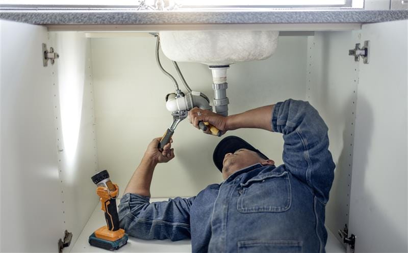 Plumber repairing pipes beneath a bathroom sink in Windsor