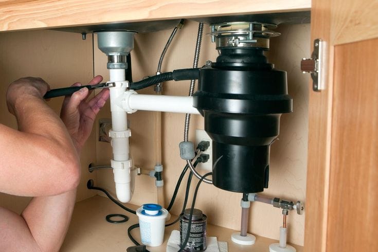 Plumber installing a garbage disposal beneath a kitchen sink in Windsor