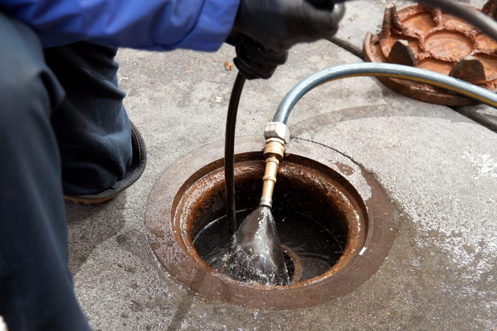 Plumber hydro jetting a sewer line through a manhole in Windsor