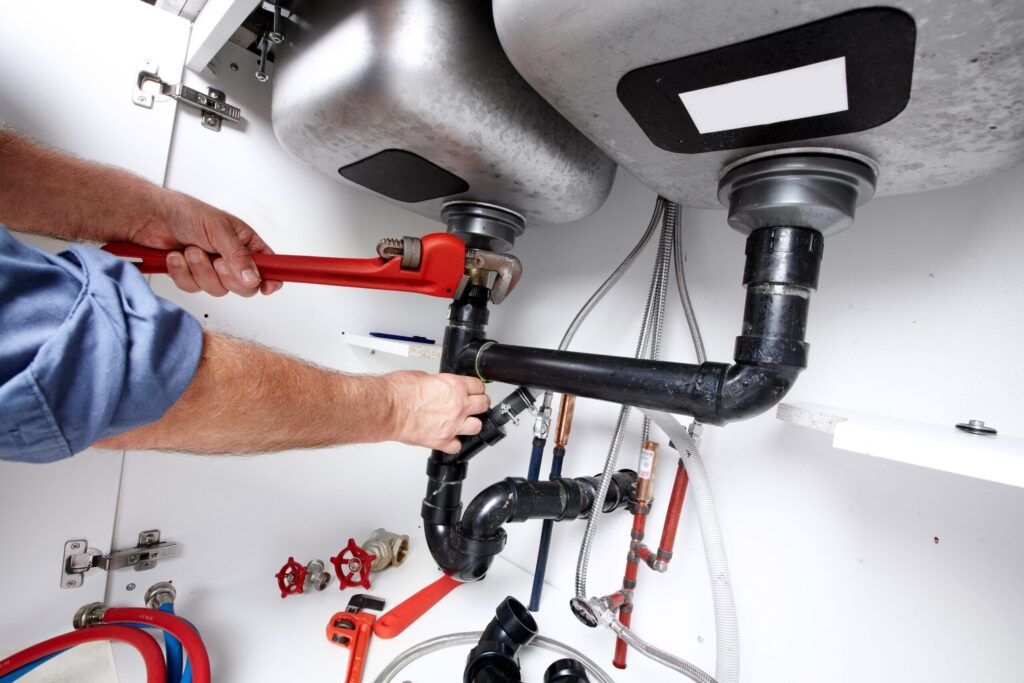 Plumber repairing drain pipes beneath a kitchen sink in Windsor